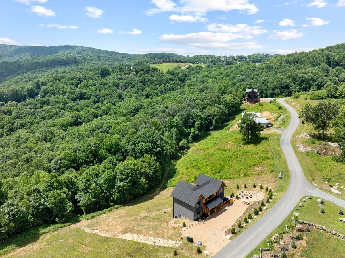 A modern house nestled among lush greenery, with a winding road leading toward the mountains. The exterior setting conveys accessibility to hiking and nature walks, and the home itself is positioned as a comfortable, welcoming base for exploration.