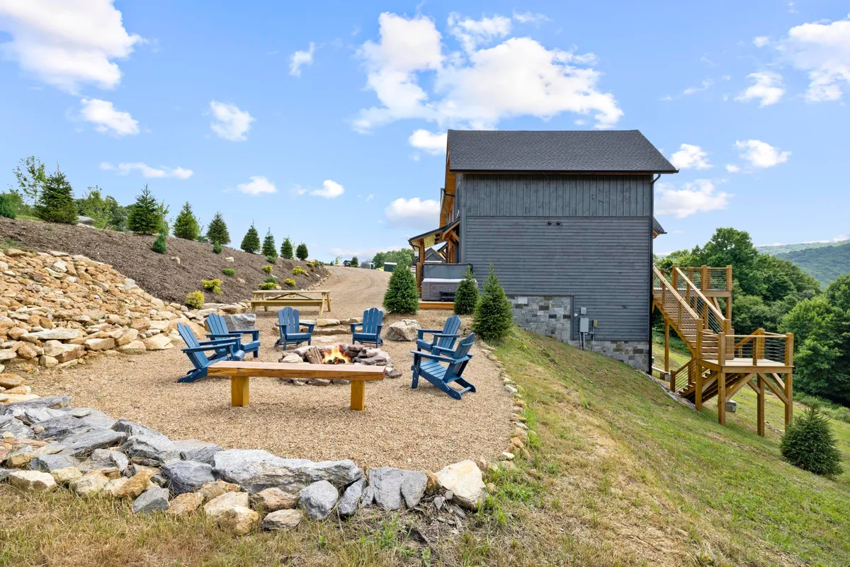 This cozy exterior shot highlights a fire pit surrounded by blue chairs on a gravel pathway, all set against a serene natural landscape. The inviting setup suggests evenings spent making s'mores, sharing stories, and enjoying mountain views with family and friends.