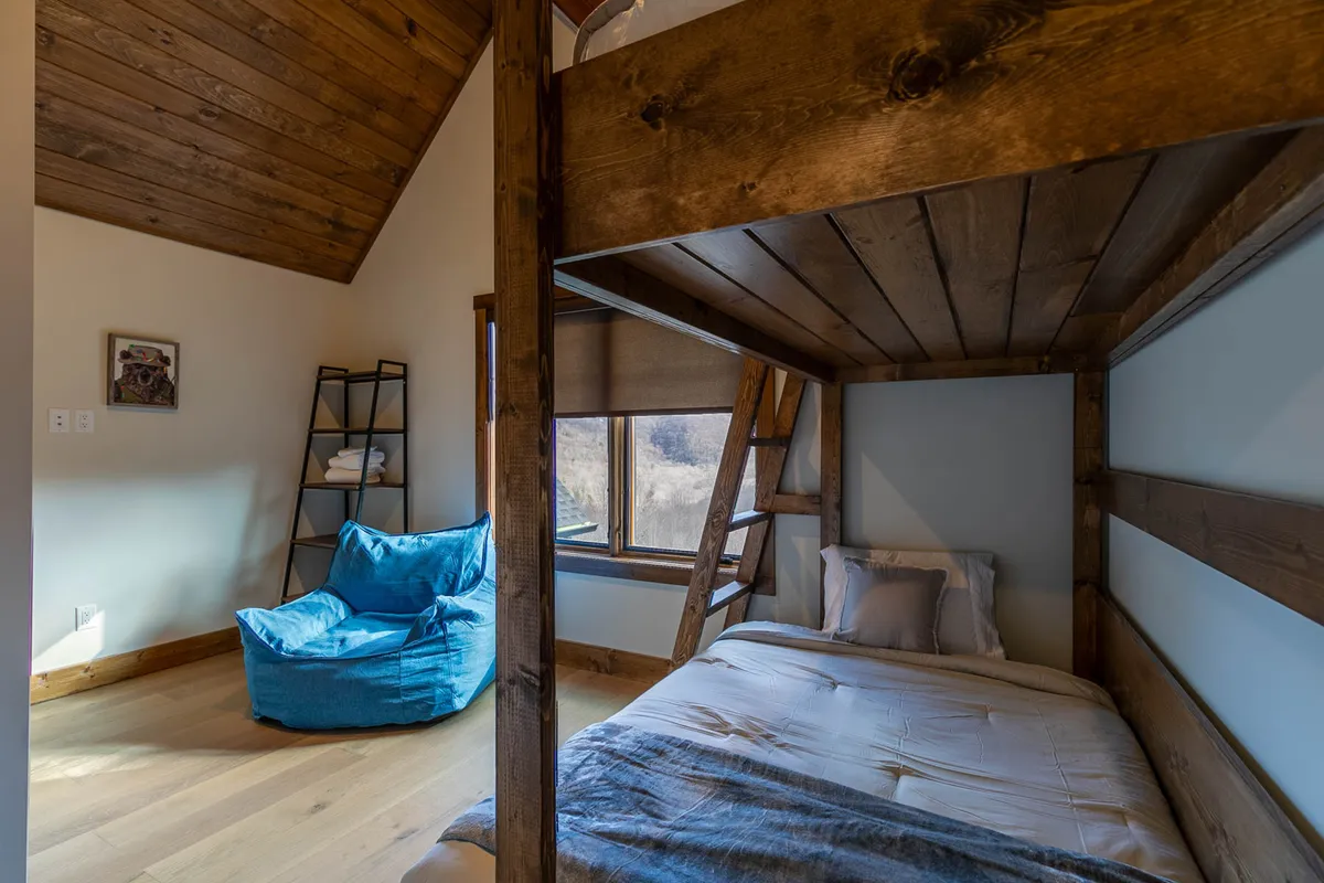A whimsical bunk bedroom outfitted with a sturdy bunk bed, a playful blue bean bag chair, and a large window that floods the space with natural light. Perfect for children or the young at heart, the room exudes a sense of coziness and fun.