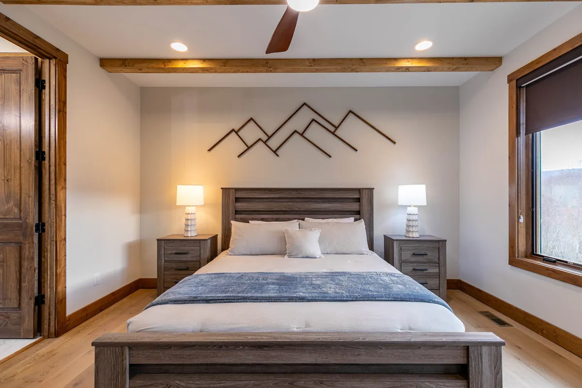 A plush king or queen bedroom featuring a cozy bed with crisp linens, mountain-themed wall art above the headboard, and soft natural light streaming in from the window. Nightstands with lamps flank the bed, creating a restful and elegant sanctuary.