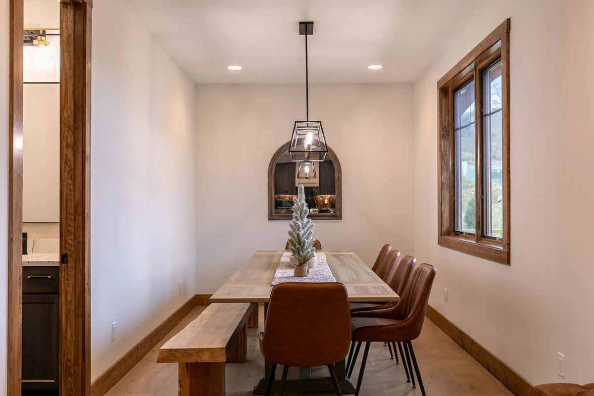 A cozy dining area featuring a sizable wooden table surrounded by comfortable chairs, ideal for hosting up to ten guests. A large decorative window and a statement light fixture create a warm, inviting atmosphere for shared meals and lively conversation.