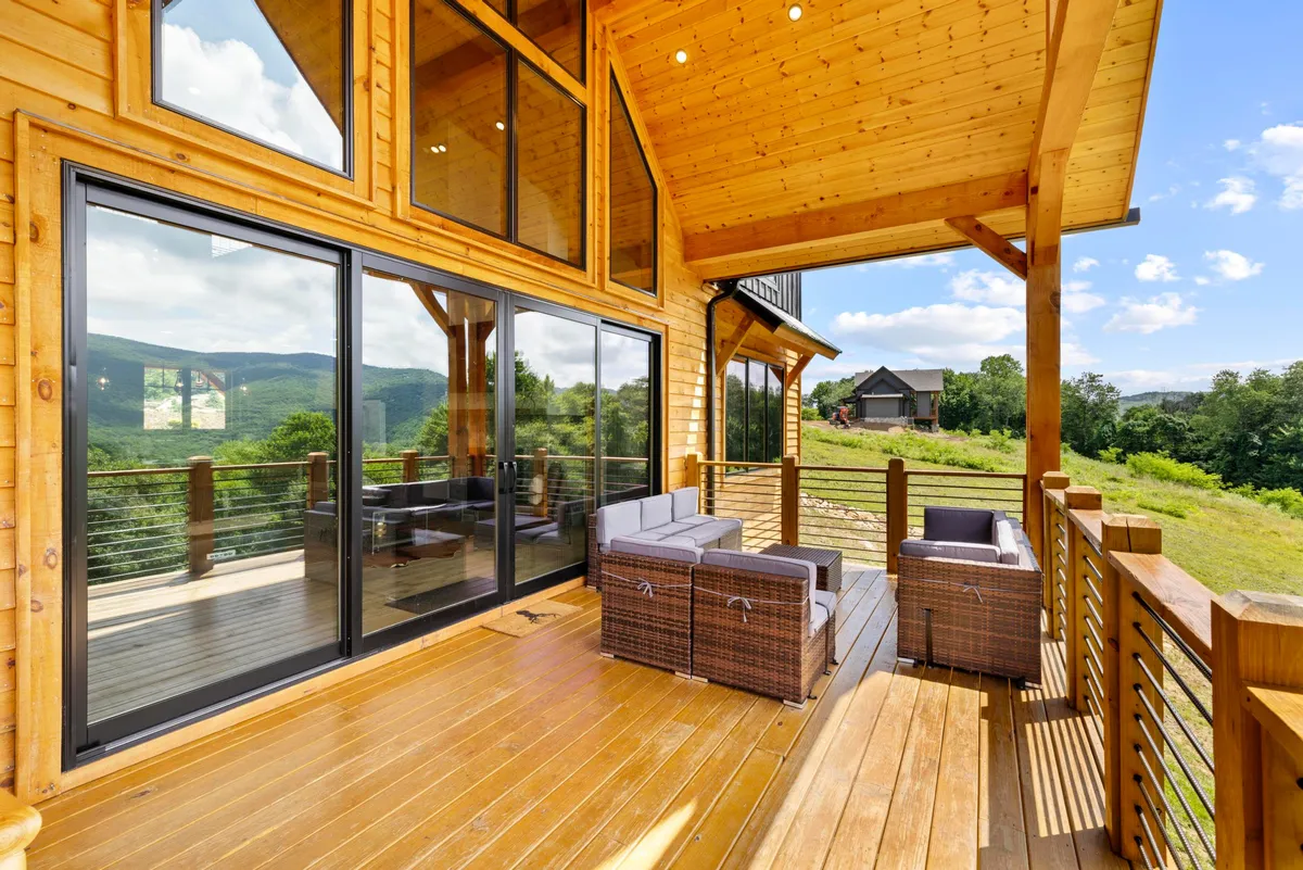 A modern lodge-style deck features large glass doors opening to an outdoor seating area, with unobstructed mountain views beyond. The arrangement is ideal for entertaining, relaxing, and enjoying nature, emphasizing seamless indoor-outdoor living.