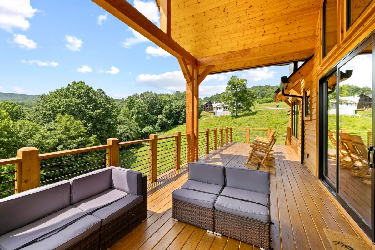 A tranquil outdoor seating area attached to a wooden structure, looking out over a lush green landscape. The space is set up for relaxation, socializing, or informal meetings, with the backdrop of rolling hills and open sky suggesting both peace and inspiration.