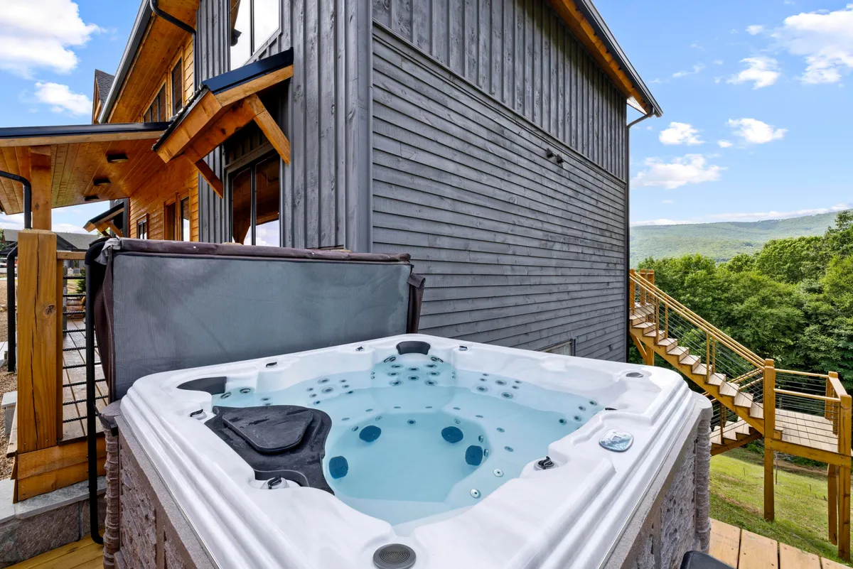A serene wooden deck with a brand-new hot tub overlooks sweeping mountain vistas. The scene evokes peaceful relaxation, with the hot tub perfectly positioned for sunset views or stargazing at night.