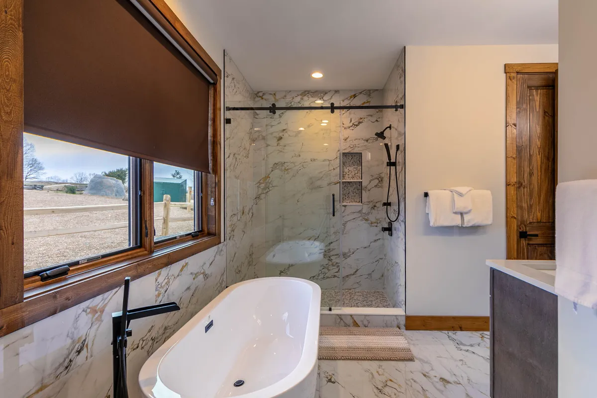 A spacious ensuite bathroom, centered on a freestanding soaking tub and an elegant glass shower enclosure. Marble walls and ample natural light add a spa-like, decadent atmosphere perfect for relaxation.