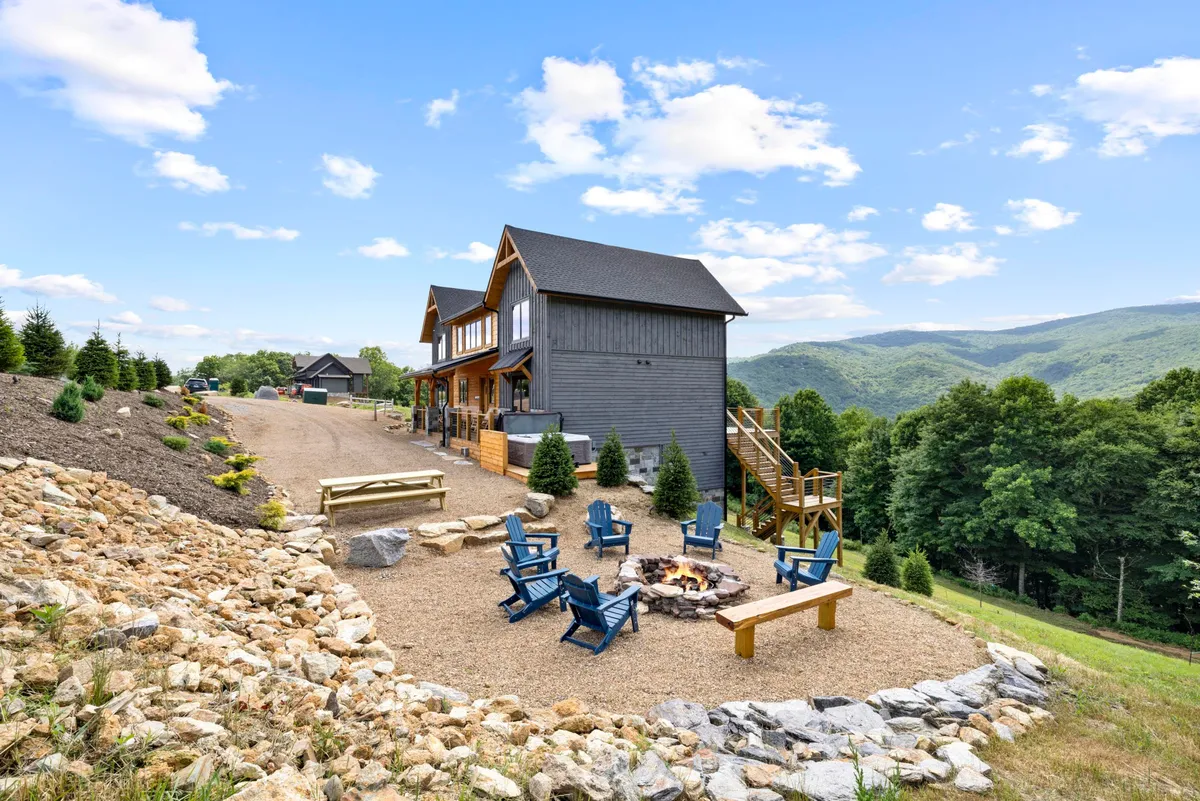 An inviting outdoor fire pit surrounded by comfortable seating on a wooden deck, with expansive landscape views and an open sky above. The scene hints at opportunities for group gatherings, campfire conversations, and stargazing, set against a serene natural backdrop.