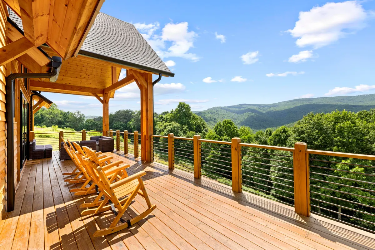 A spacious wooden deck furnished with classic rocking chairs, overlooking an expansive mountain vista. The scene suggests a tranquil spot ideal for group relaxation or lively gatherings, with the natural beauty of the mountains forming a breathtaking backdrop.
