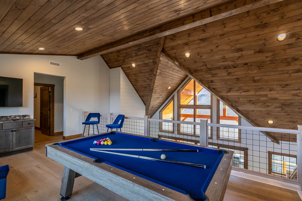 This image offers another angle of the entertainment loft, highlighting a spacious area with a pool table at its center. The loft's high wooden ceilings and expansive windows create a bright, airy ambiance, while the arrangement encourages both group play and casual relaxation.